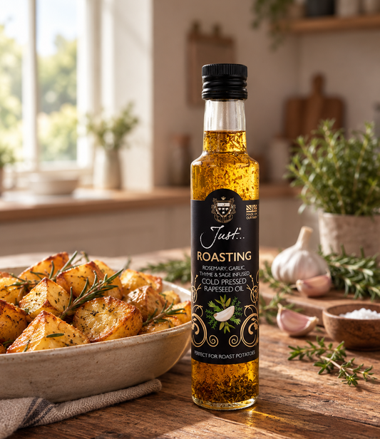 Bottle of Just Oil Roasting cold-pressed rapeseed oil infused with rosemary, garlic, thyme and sage, beside a bowl of golden roast potatoes